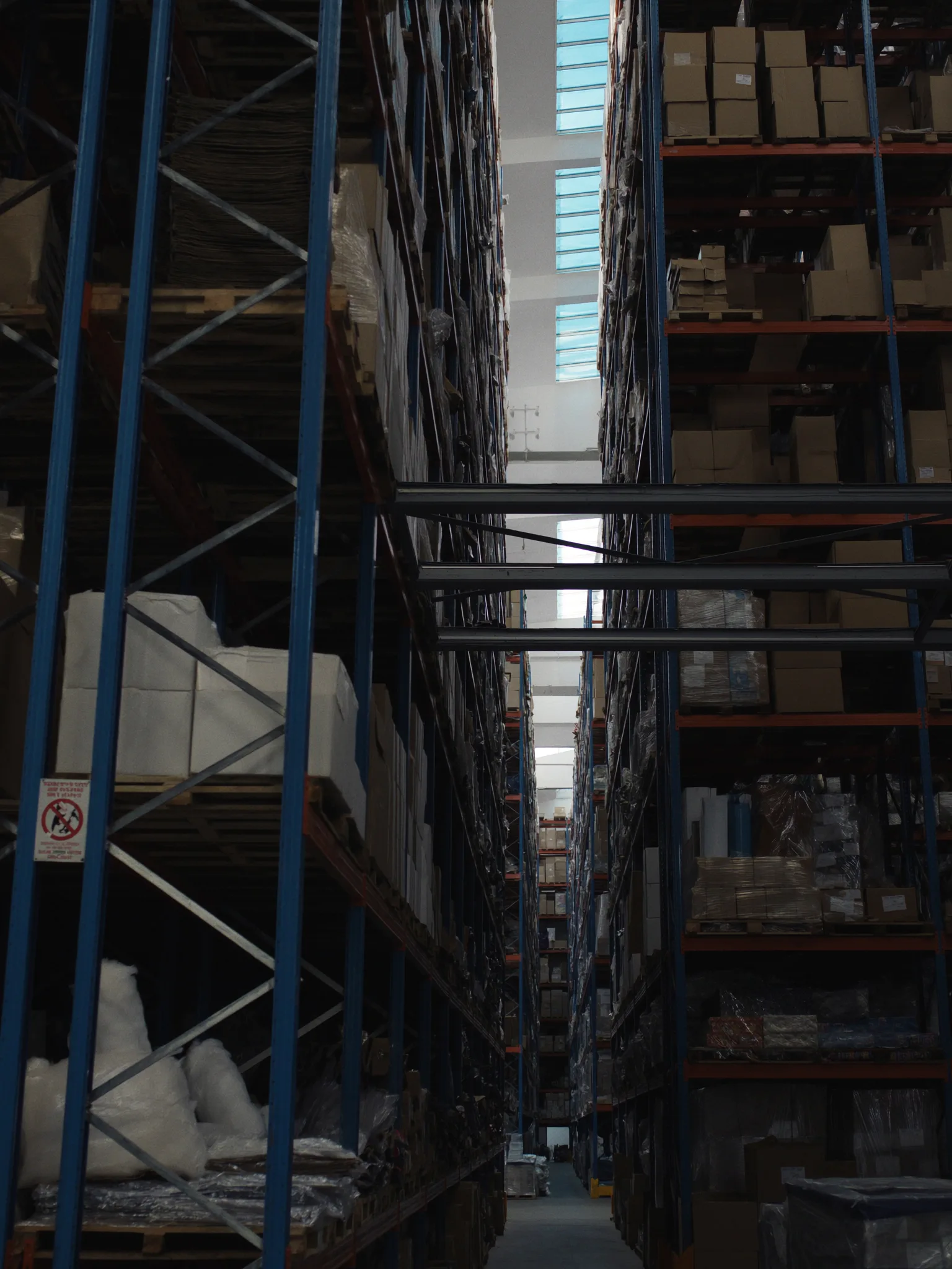 Pasillo entre dos estanterías rack altas cargadas con mercancía variada en un almacén industrial